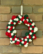 Colorful felt ball wreath hanging on a brick wall