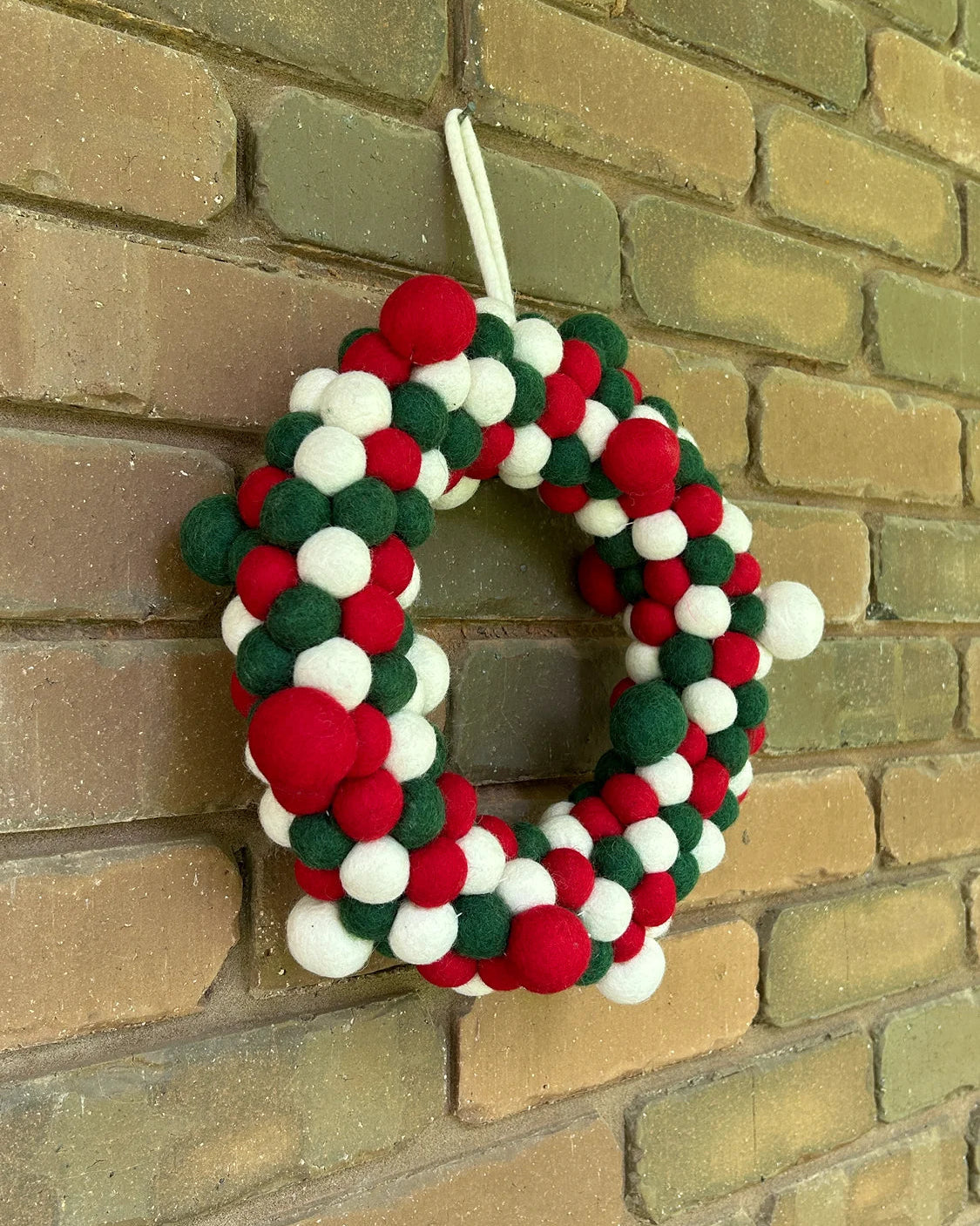 Decorative wreath with red, green, and white balls hanging on a brick wall.