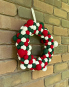 Decorative wreath with red, green, and white balls hanging on a brick wall.
