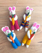 Four crocheted bunny toys with colorful overalls and carrots on a wooden surface