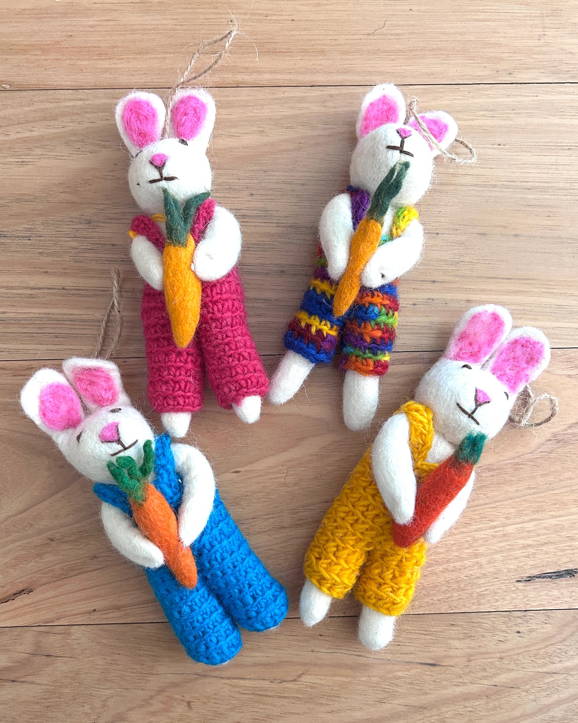 Four crocheted bunny toys with colorful overalls and carrots on a wooden surface