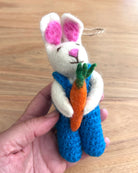 Handmade felt rabbit toy with a carrot held by a person on a wooden surface