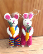 Two knitted rabbits with colorful overalls and carrots on a wooden surface.