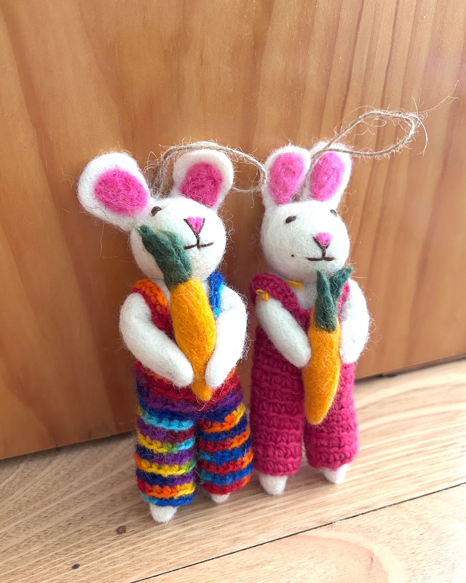 Two crocheted rabbit toys with colorful overalls and carrots on a wooden surface.