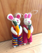 Two crocheted rabbit toys with colorful overalls and carrots on a wooden surface.