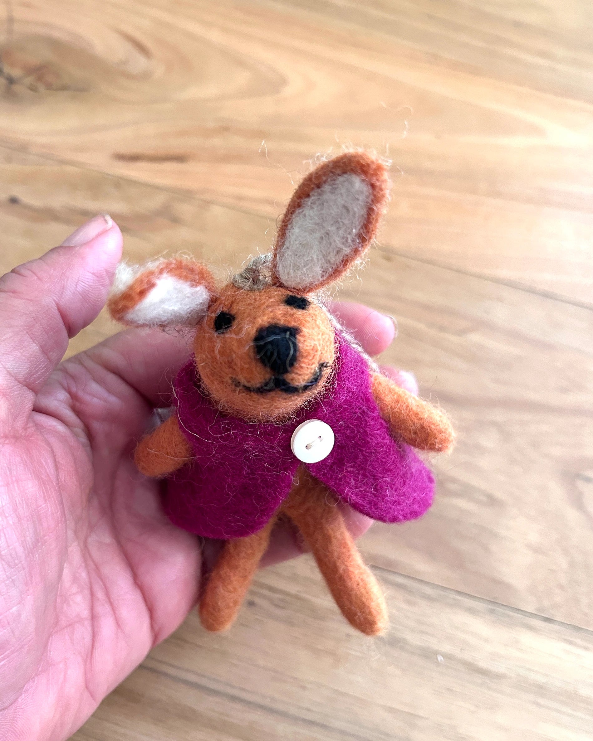 Small felt rabbit toy in a pink coat held in a hand on a wooden surface