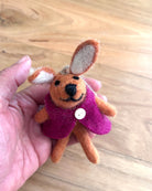 Small felt rabbit toy in a pink coat held in a hand on a wooden surface