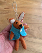 Small felt rabbit ornament with a blue sweater held in a hand on a wooden surface