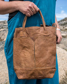 Person holding a brown leather bag in a desert landscape