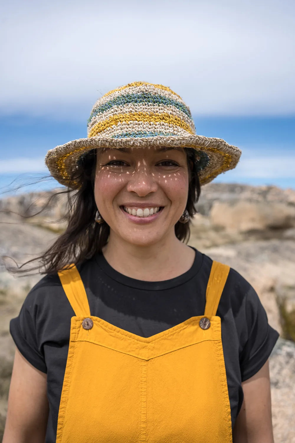 Person wearing a straw hat and yellow overalls standing outdoors with a blue sky background