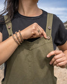 Person wearing a black shirt and green overalls with a blurred natural background