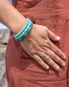 Person wearing a turquoise bracelet and ring with a natural landscape background