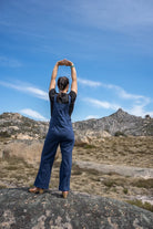 Person in blue overalls standing on a rock with mountains and clear sky in the background