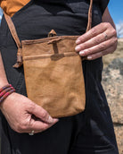 Person holding a brown leather pouch outdoors with a scenic background