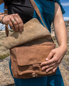 Person holding a brown leather bag in a natural outdoor setting