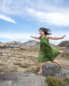 Woman in a green dress standing on a rock with mountains and blue sky in the background