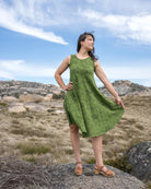 Woman in a green dress standing on a rocky landscape with a blue sky.