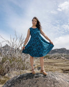 Woman in a blue dress standing on a rock with a mountainous landscape in the background