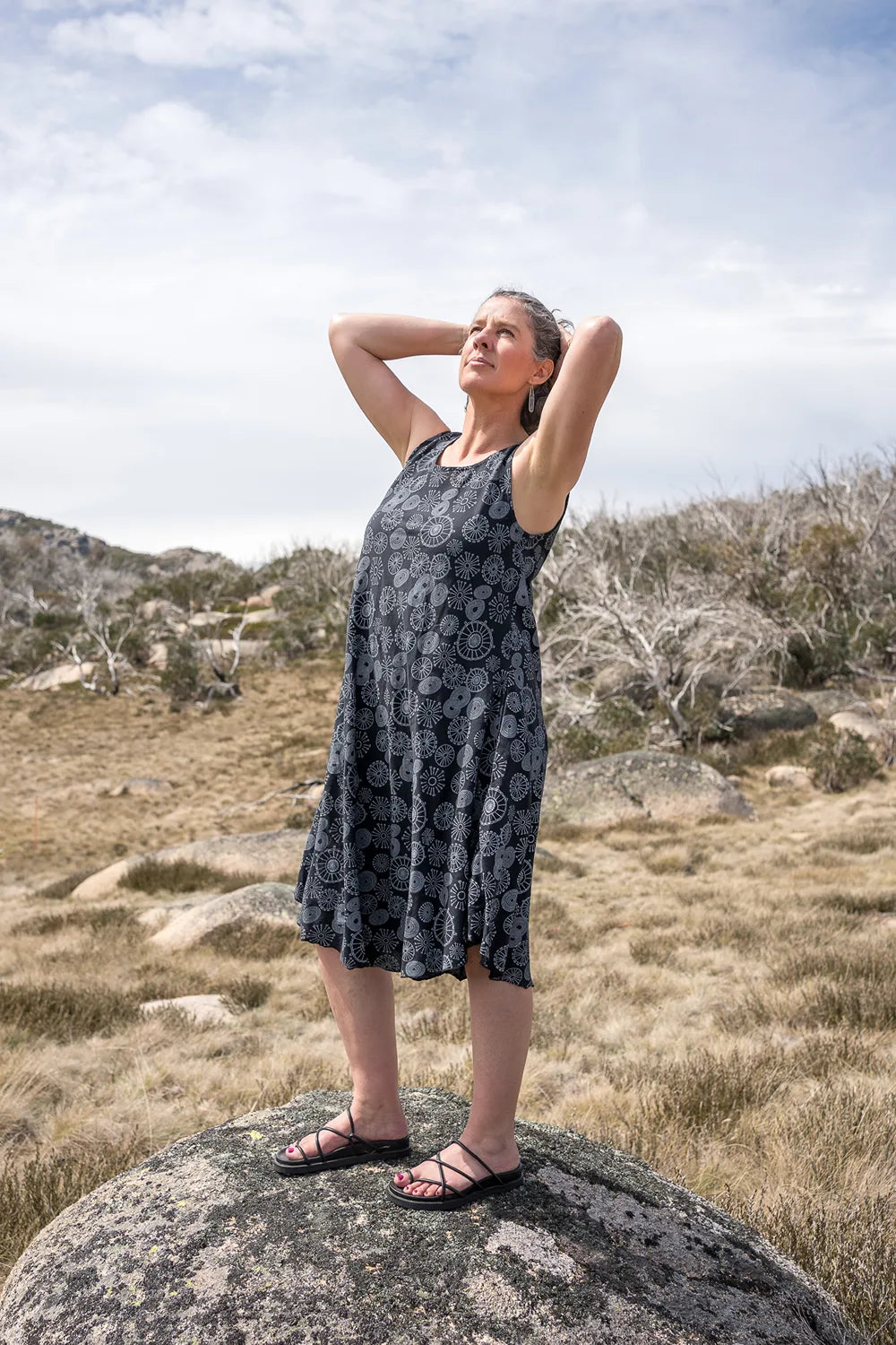 Woman in a sleeveless dress standing on a rock in a natural landscape