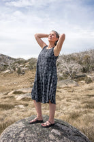 Woman in a sleeveless dress standing on a rock in a natural landscape