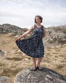 Woman in a sleeveless black print dress standing on a rock in a natural landscape