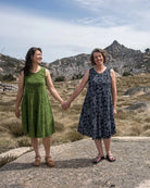 Two women holding hands on a rocky outcrop with mountains in the background