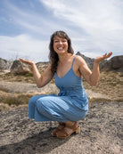 Woman in a blue dress squatting outdoors with a clear sky and rocky landscape.