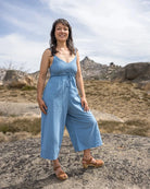 Woman in a blue jumpsuit standing on a rocky landscape with mountains in the background