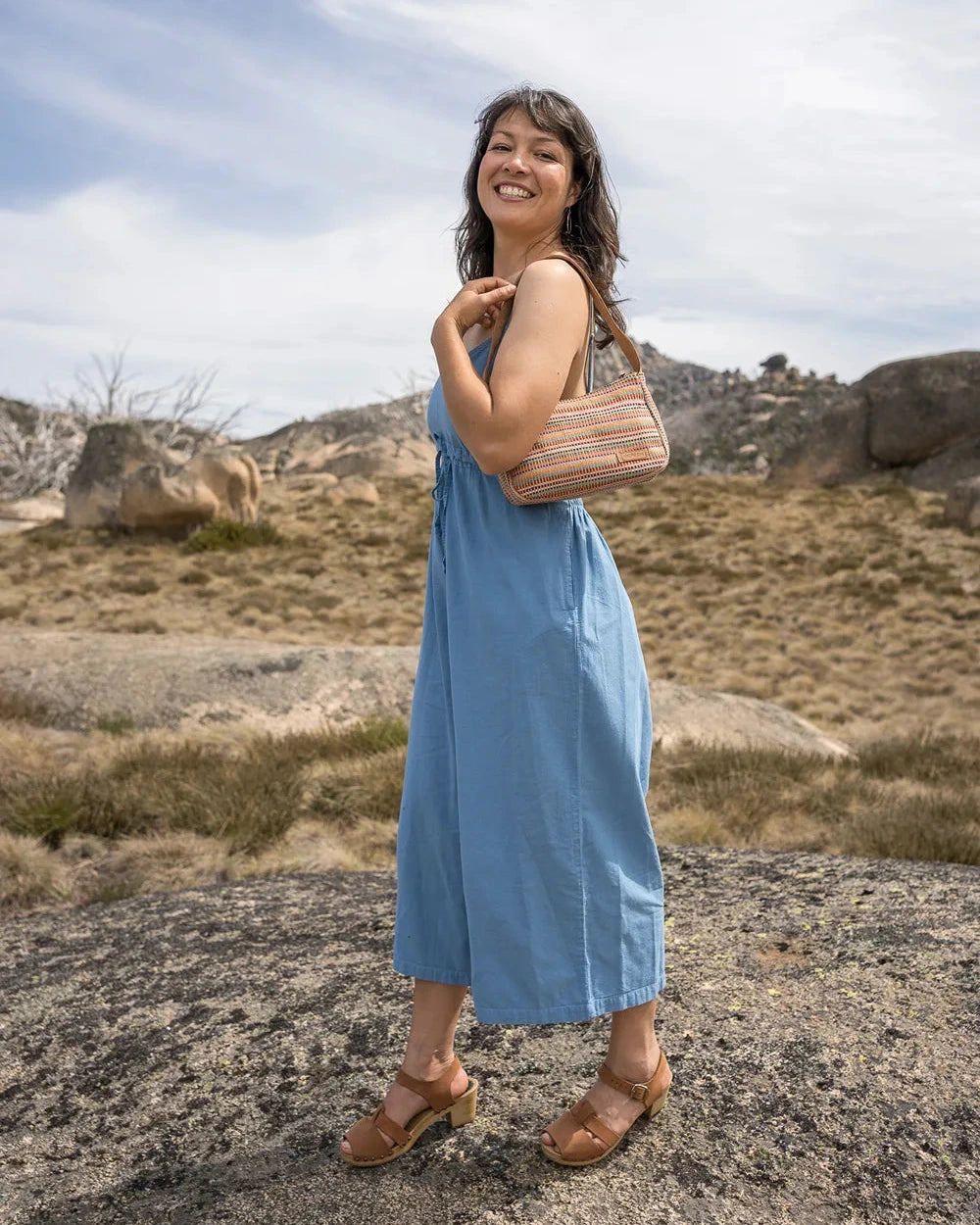 Woman in a romper  holding a brown bag in a desert landscape