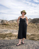 Woman in a black jumpsuit and hat standing on a rocky landscape with a blue sky.