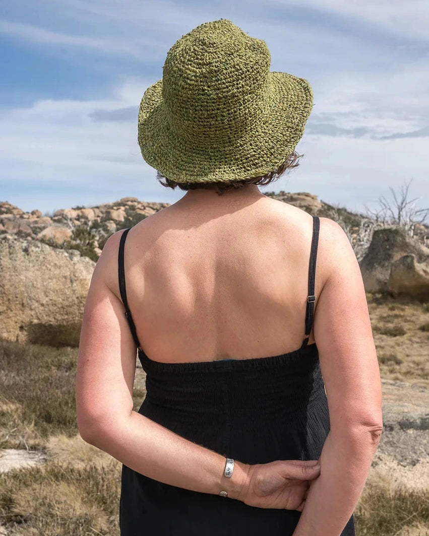 Person wearing a green hat and black jumpsuit standing in a desert landscape