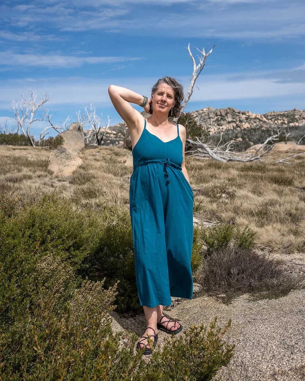 Woman in a blue romper standing in a desert landscape with a clear sky.