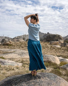 Person standing in a blue ruffle skirt with a scenic background of mountains and sky.