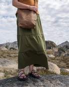 Woman standing outdoors with a brown bag against a cloudy sky