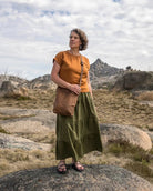 Woman in a green skirt standing on a rocky landscape with mountains in the background
