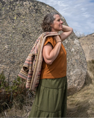 Woman in rust and khaki colour clothes standing outdoors with a large rock and blue sky in the background