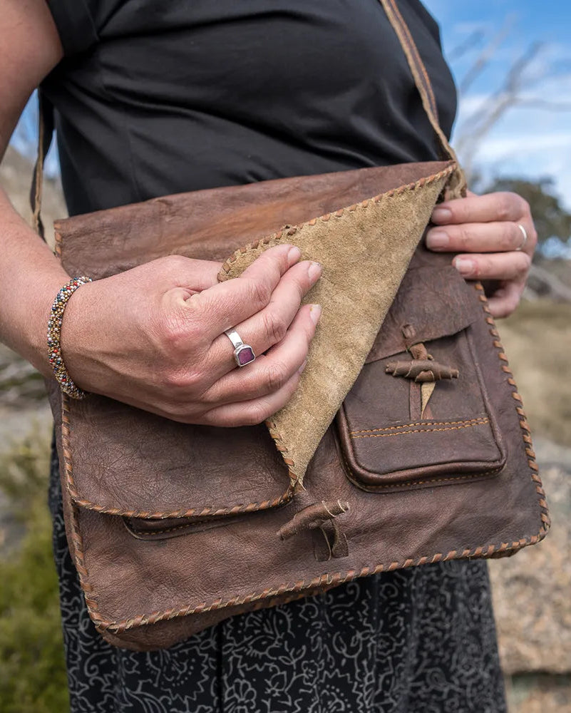 Person holding a brown leather bag outdoors with a mountainous background