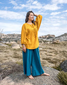 Woman in a yellow top and blue pants standing on a rock with a scenic background