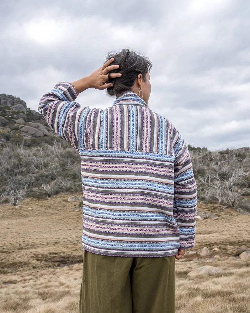 Person wearing a striped jacket and wide-leg pants standing on a rock with a landscape in the background