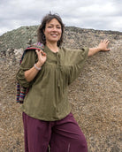 Woman in a green top and purple pants standing against a rocky background