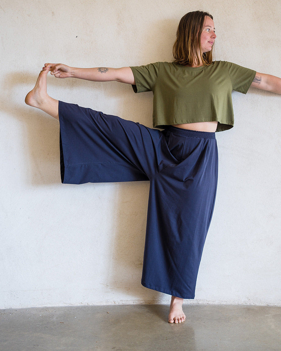 A woman in a yoga pose wearing an olive green cropped t-shirt and Sky Gypsies navy blue wide-leg pants.