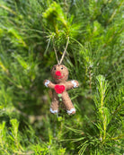 Handmade ornament shaped like a figure with red hearts hanging on a green tree.