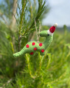 Green felt dinosaur ornament with red spots and a Santa hat hanging on a tree.
